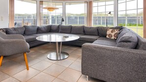 Ein modernes Wohnzimmer mit einem Ecksofa, einem runden Couchtisch und großen Fenstern mit Blick ins Freie.