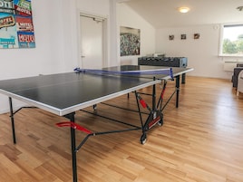 Una mesa de ping pong en una habitación con suelo de madera, una puerta y un ventanal.