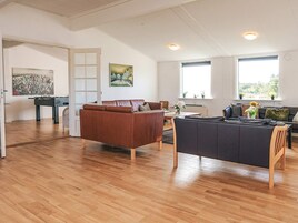 Amplia sala de estar con un sofá marrón, un sofá oscuro y una mesa de centro de madera. Hay un cuadro en la pared y una ventana con vistas a zonas verdes.