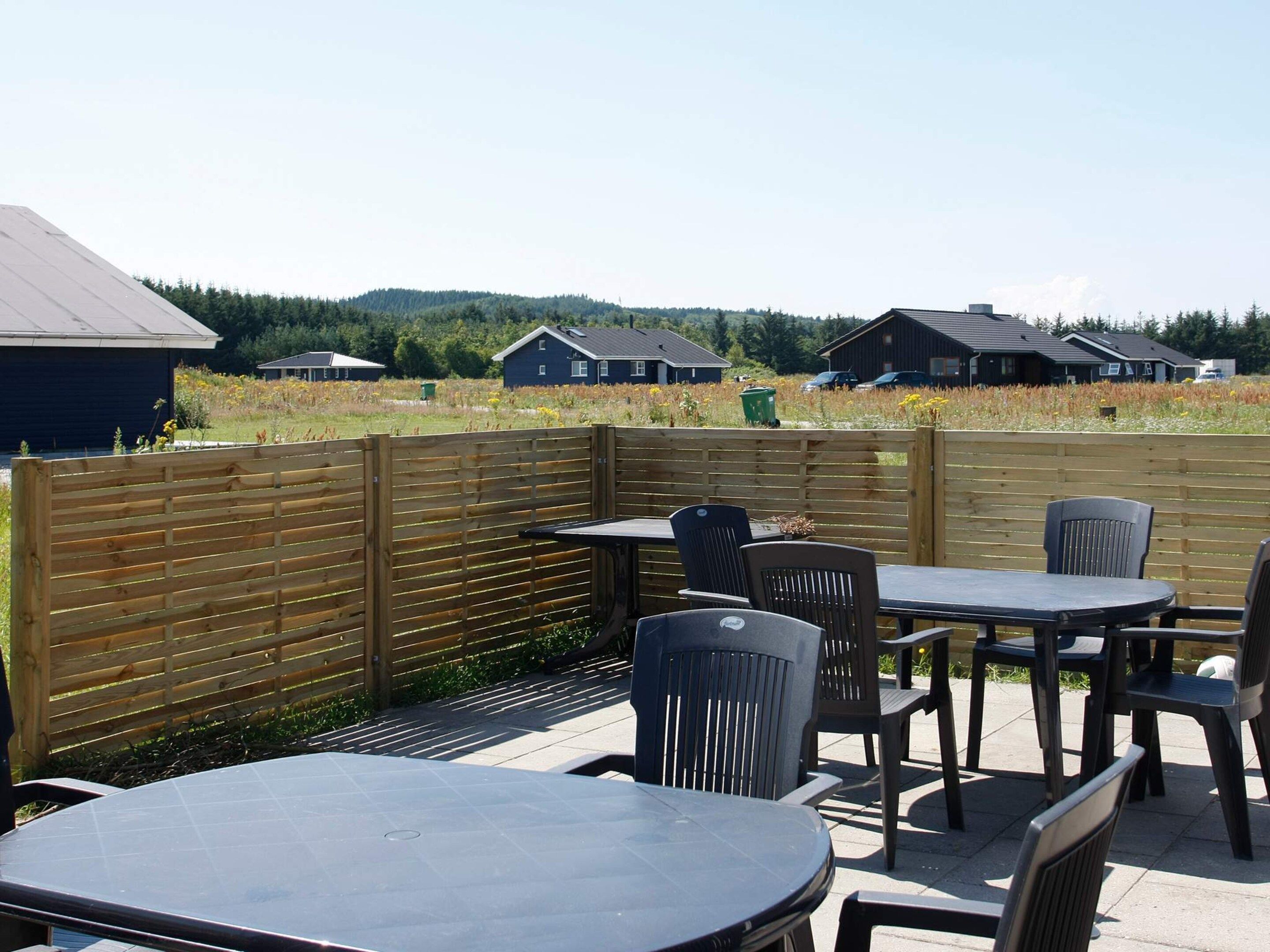 An outdoor patio area with tables and chairs, a wooden fence, and houses in the background.