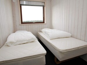 Una habitación pequeña con dos camas individuales, cada una con colchón y almohada. Hay una ventana con persianas sobre las camas.