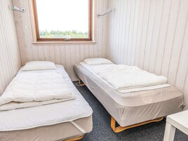 Un alojamiento pequeño, de una sola habitación, con dos camas, una ventana y una mesa blanca.