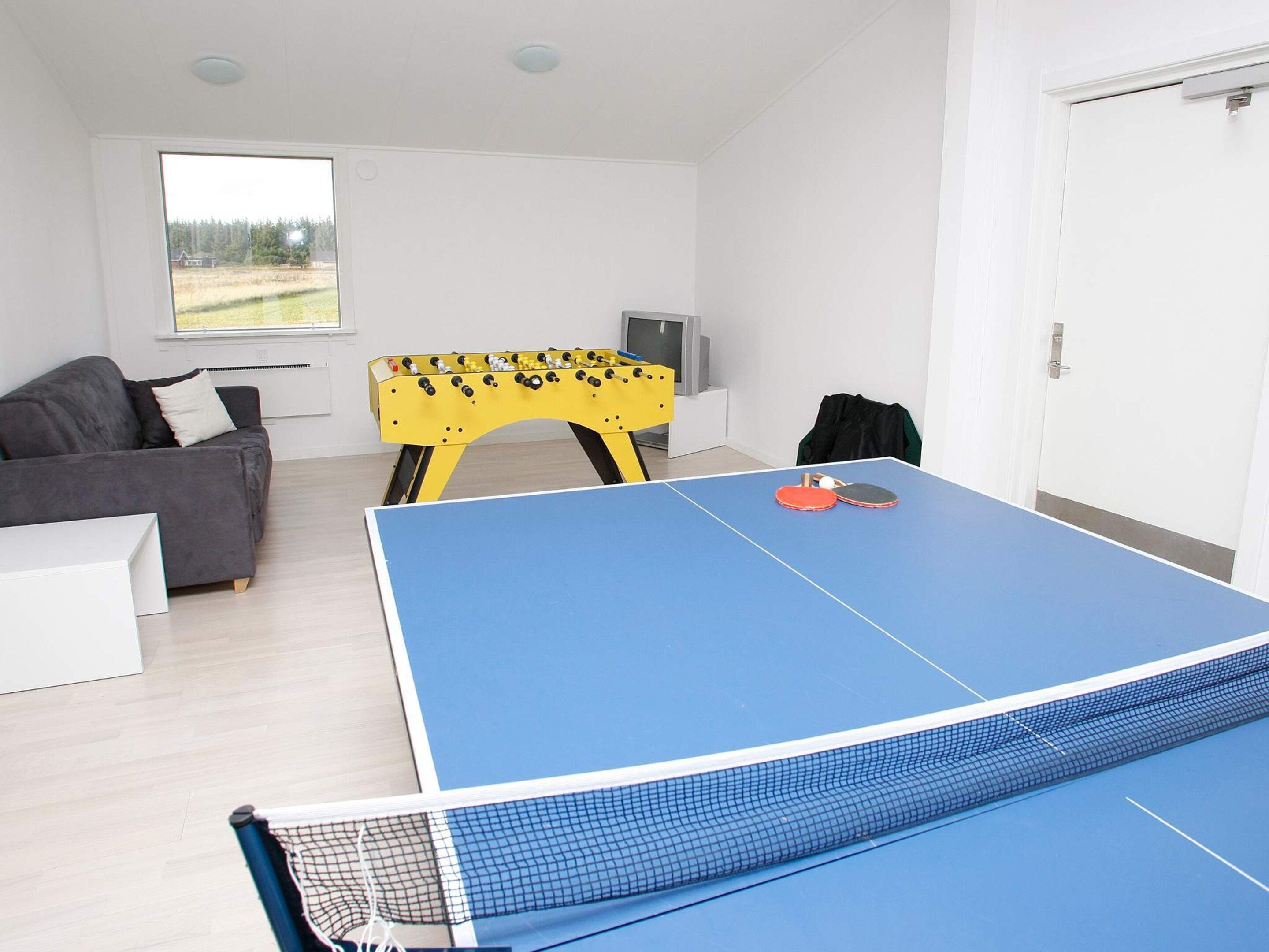 A room with a ping pong table, a sofa, a foosball table, and a television.
