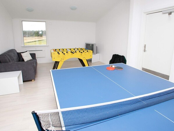 A room with a ping pong table, a sofa, a foosball table, and a television.