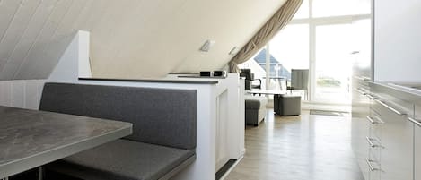 A modern loft-style room with a dining area, kitchenette, and a large window providing natural light.