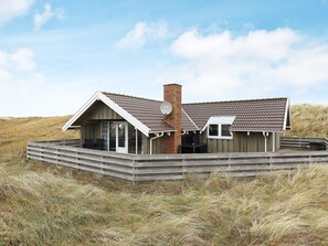 A coastal house with a wooden deck, a brick chimney, and a glass door entrance.