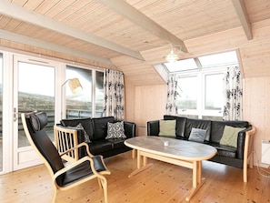 A cozy room with a wooden ceiling, two black leather sofas, a wooden table, and a chair.