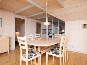 A wooden dining room with a round table and chairs, a hanging light fixture, and a view into the kitchen area. - 4 Star Holiday Home in Ringkobing (Ringkobing)