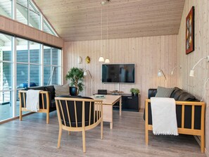 Un salon moderne avec des murs recouverts de panneaux en bois, un téléviseur à écran plat, une table à manger et deux canapés agrémentés de plaids.