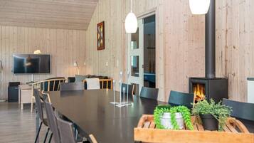 Een modern interieur met een lange eettafel, stoelen, een flatscreen televisie, een open haard en houten wanden.