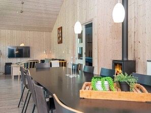 Un interior moderno con una larga mesa de comedor, sillas, un televisor de pantalla plana, chimenea y paredes de madera.