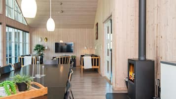 A modern interior with a long dining table, chairs, a TV, and a wood-burning stove.