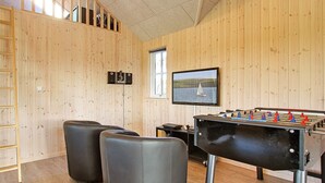 Habitación con paredes de madera, mesa de futbolín, dos otomanes negros, ventana con vista al mar y televisor montado.