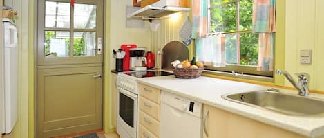 Cocina compacta con estufa, horno y pileta, muebles de madera y un ventanal con cortinas.