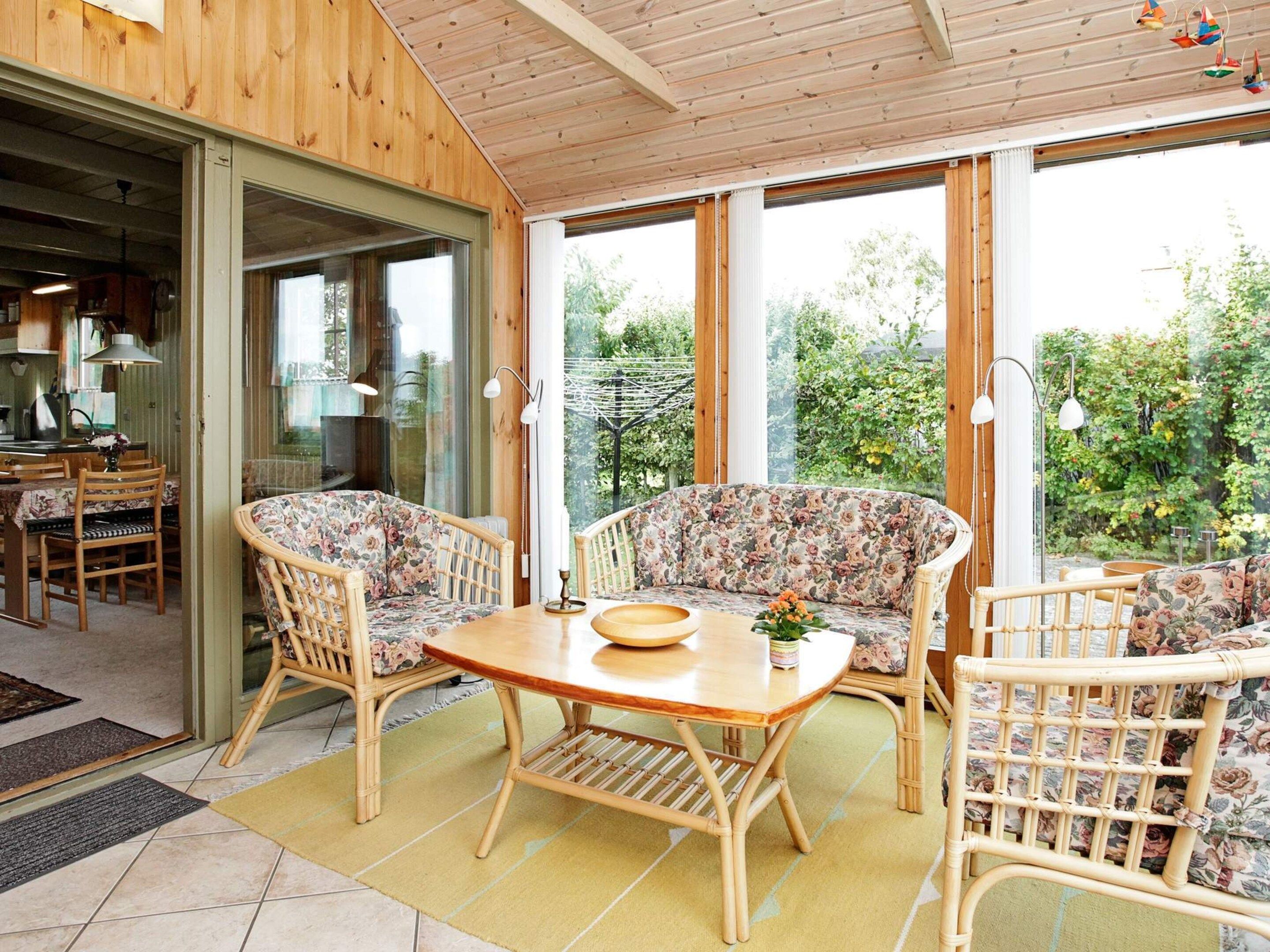 A cozy room with a wooden ceiling, a large window, a dining table with chairs, and a sofa with floral upholstery.