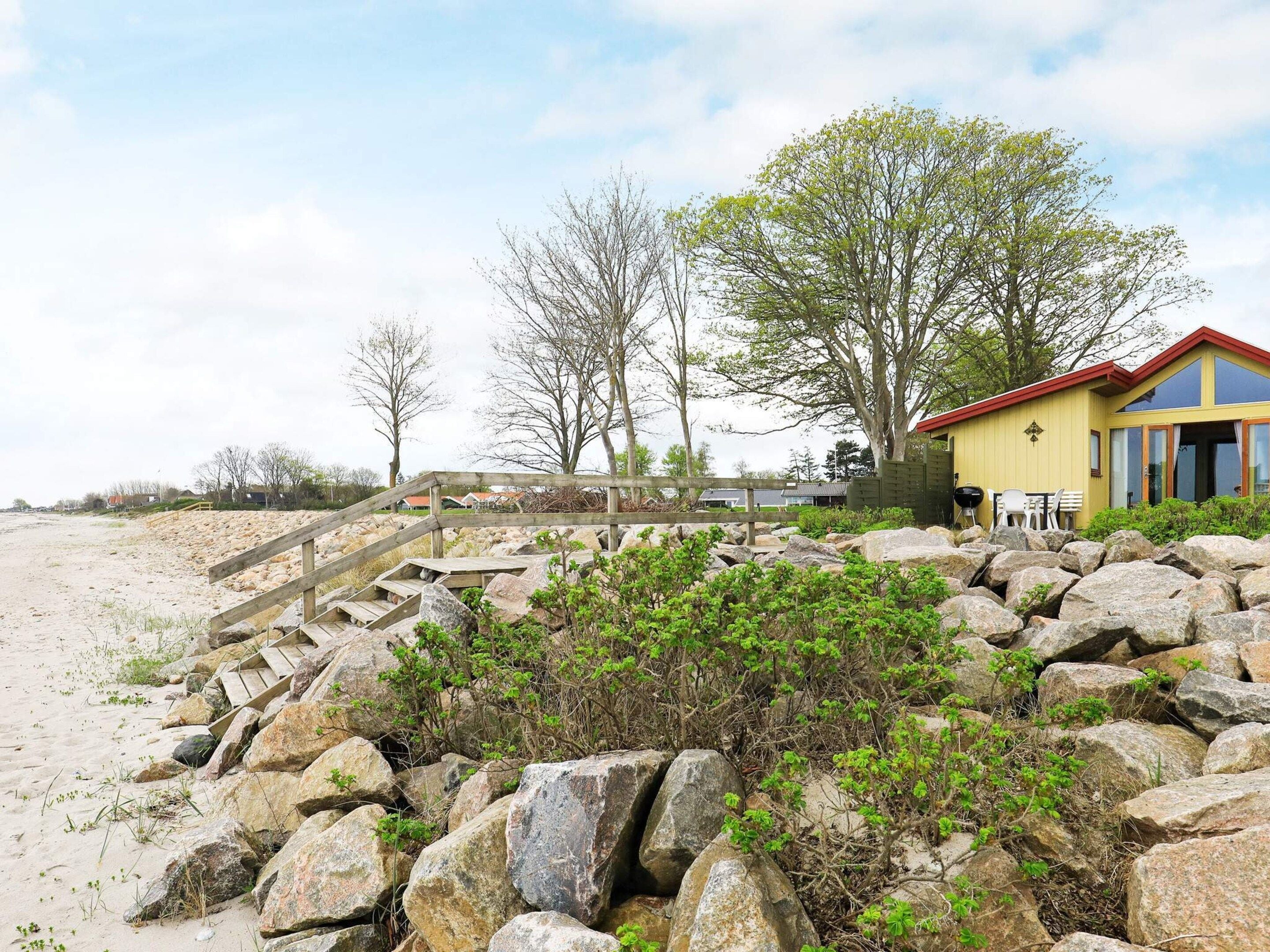 A beachside property with a wooden staircase leading to a yellow building, surrounded by large rocks and sparse vegetation.