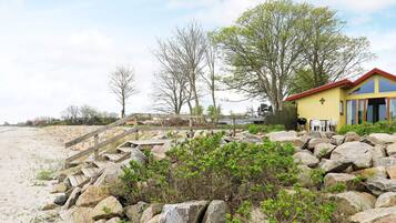 A beachside property with a wooden staircase leading to a yellow building, surrounded by large rocks and sparse vegetation.