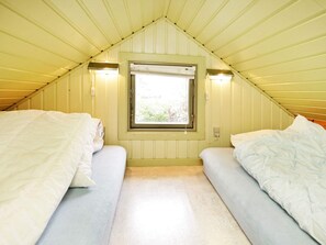 A small, single-room accommodation with a sloped ceiling, two beds, a window, and wall-mounted lights.