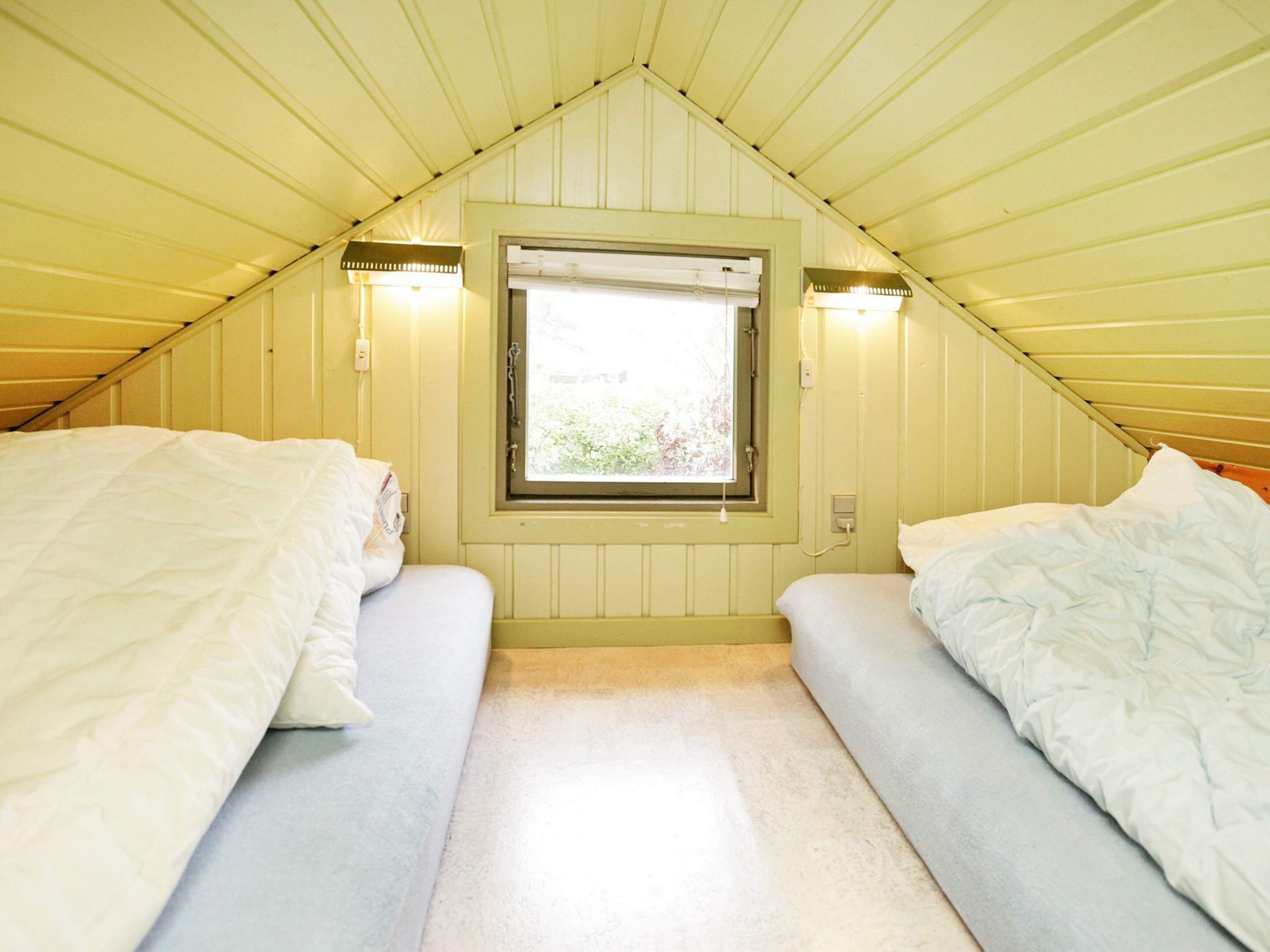 A small, single-room accommodation with a sloped ceiling, a window with a view, and two beds.