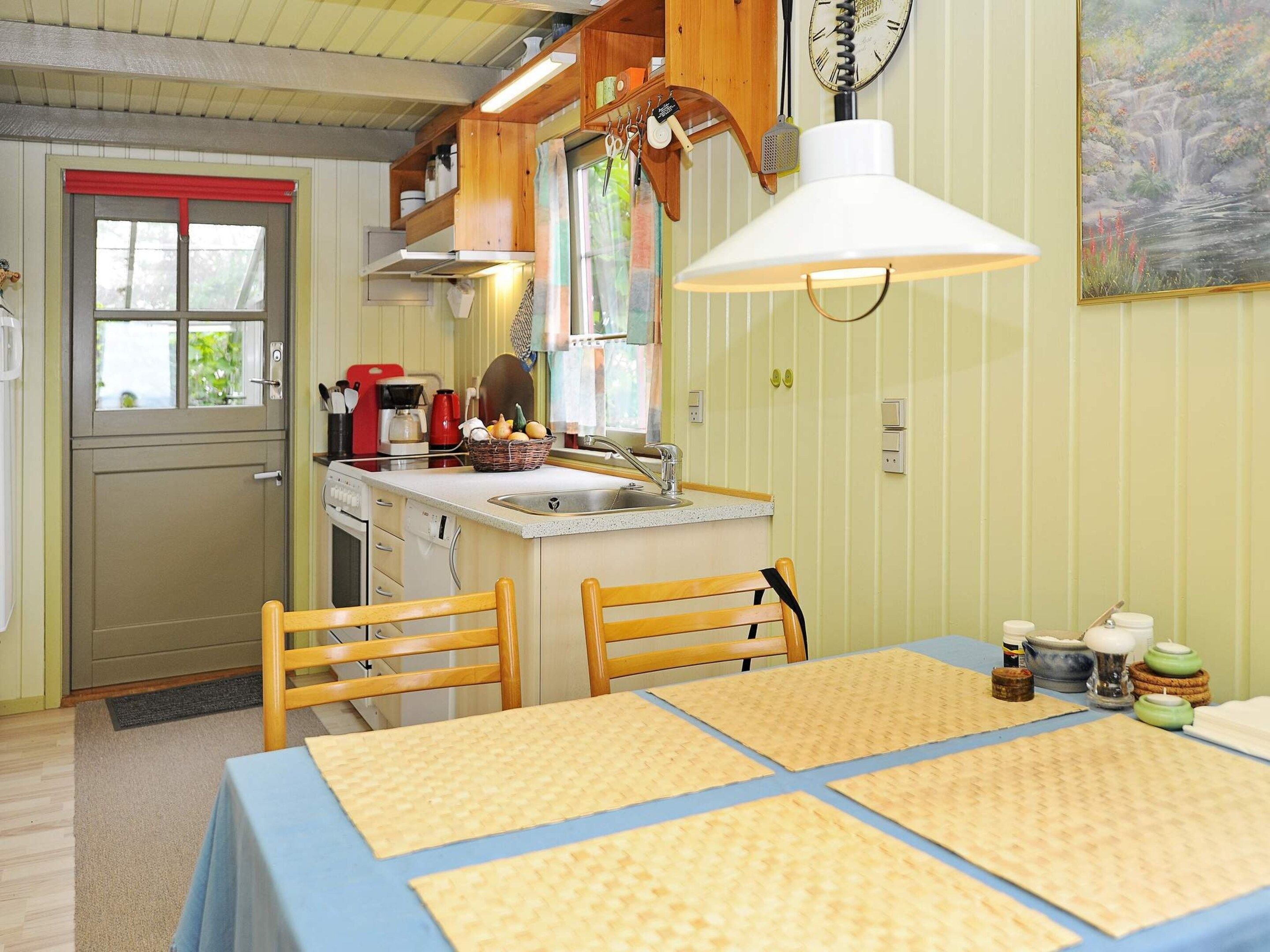 Una cocina compacta con comedor, sillas de madera, una mesa con individuales y una lámpara colgante.