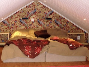 A bedroom with a sloped ceiling, floral wallpaper, a bed with a floral blanket, and a nightstand with a lamp. - 4 Person Holiday Home in Unnaryd (Unnaryd)