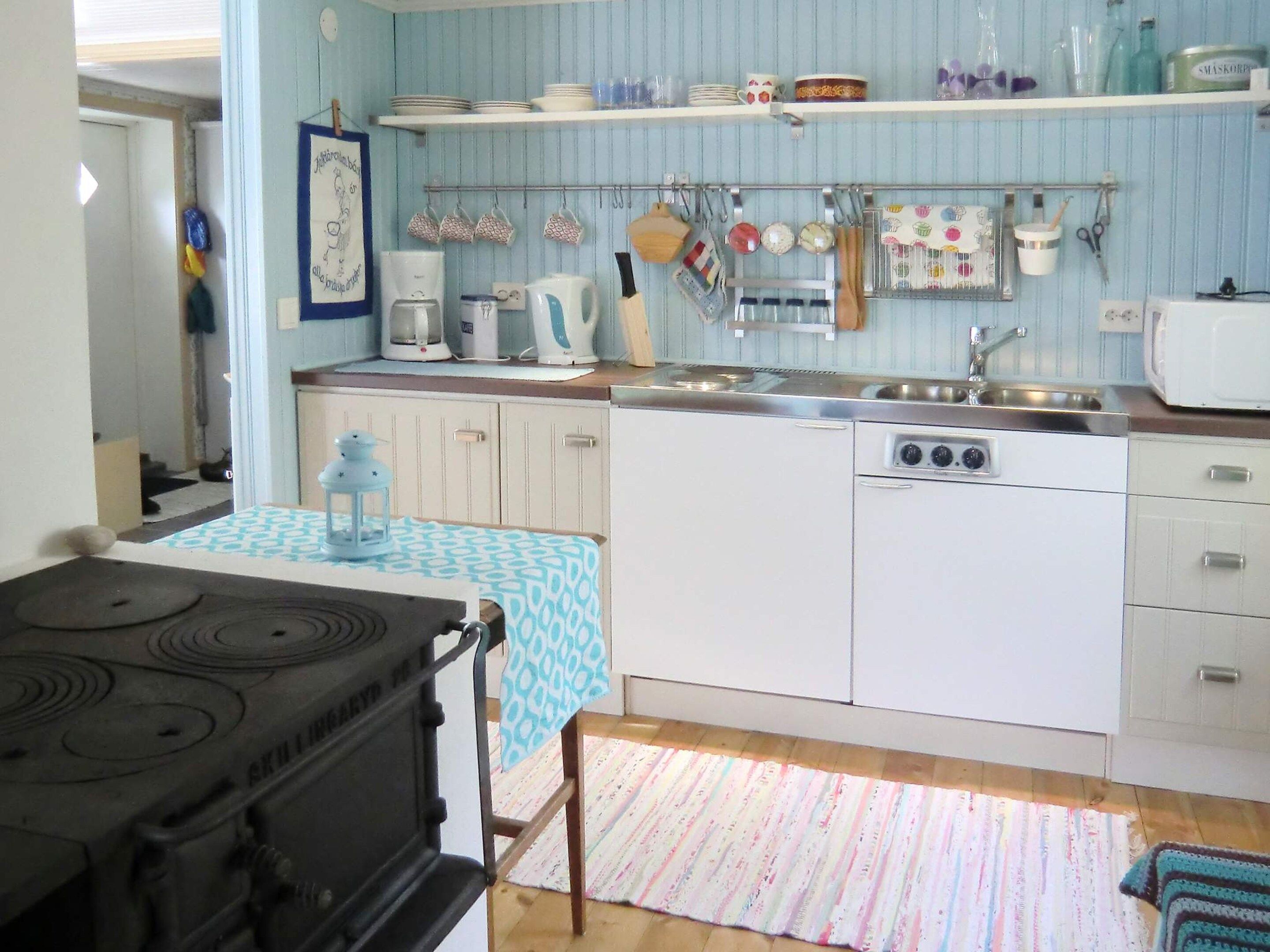 A compact kitchen with a stove, sink, and a microwave. There are cabinets and a small table with a patterned tablecloth.