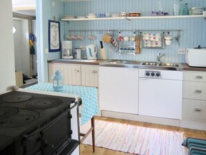 Een kleine keuken met een fornuis, gootsteen en een magnetron. Uitsluitend kastjes en een tafeltje met een tafelkleed met dessin.