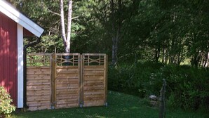 Un espace clos délimité par une clôture et doté d’un portail en bois, un petit jardin agrémenté d’une structure en pierre et un bâtiment rouge.