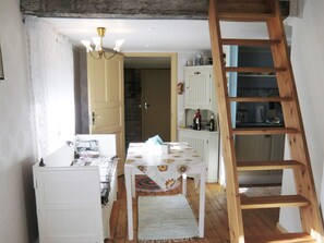 Une pièce avec une échelle en bois, une table recouverte d’une nappe à motifs floraux et une porte donnant sur une autre pièce.