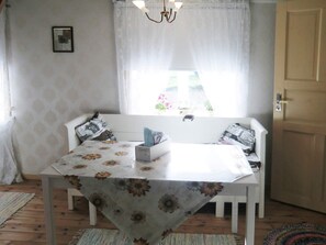 A dining area with a table covered in a floral tablecloth, a bench with patterned cushions, and a window with sheer curtains. - 4 Person Holiday Home in Unnaryd (Unnaryd)