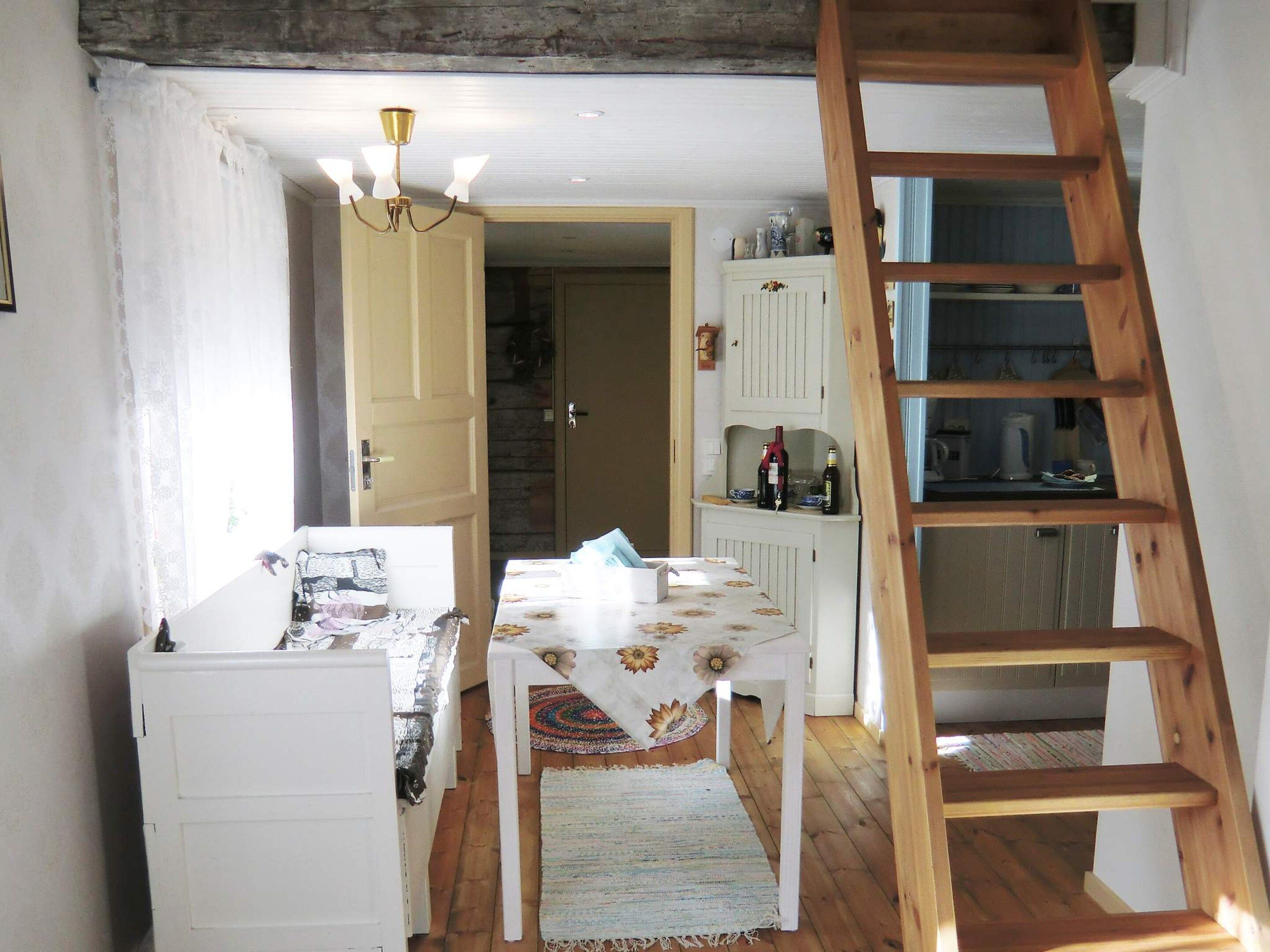 A room with a wooden ladder, a table with a floral tablecloth, and a white cabinet with wine bottles.