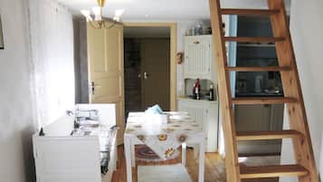 A room with a wooden ladder, a table with a floral tablecloth, and a white cabinet with wine bottles.