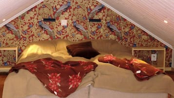 A bedroom with a sloped ceiling, a bed with floral bedding, and a wall with a peacock pattern.