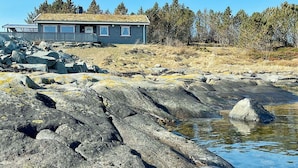 A house with a sloped roof, a deck, and a view of a rocky shoreline with water. - Holiday Home in Storfosna (Orland)