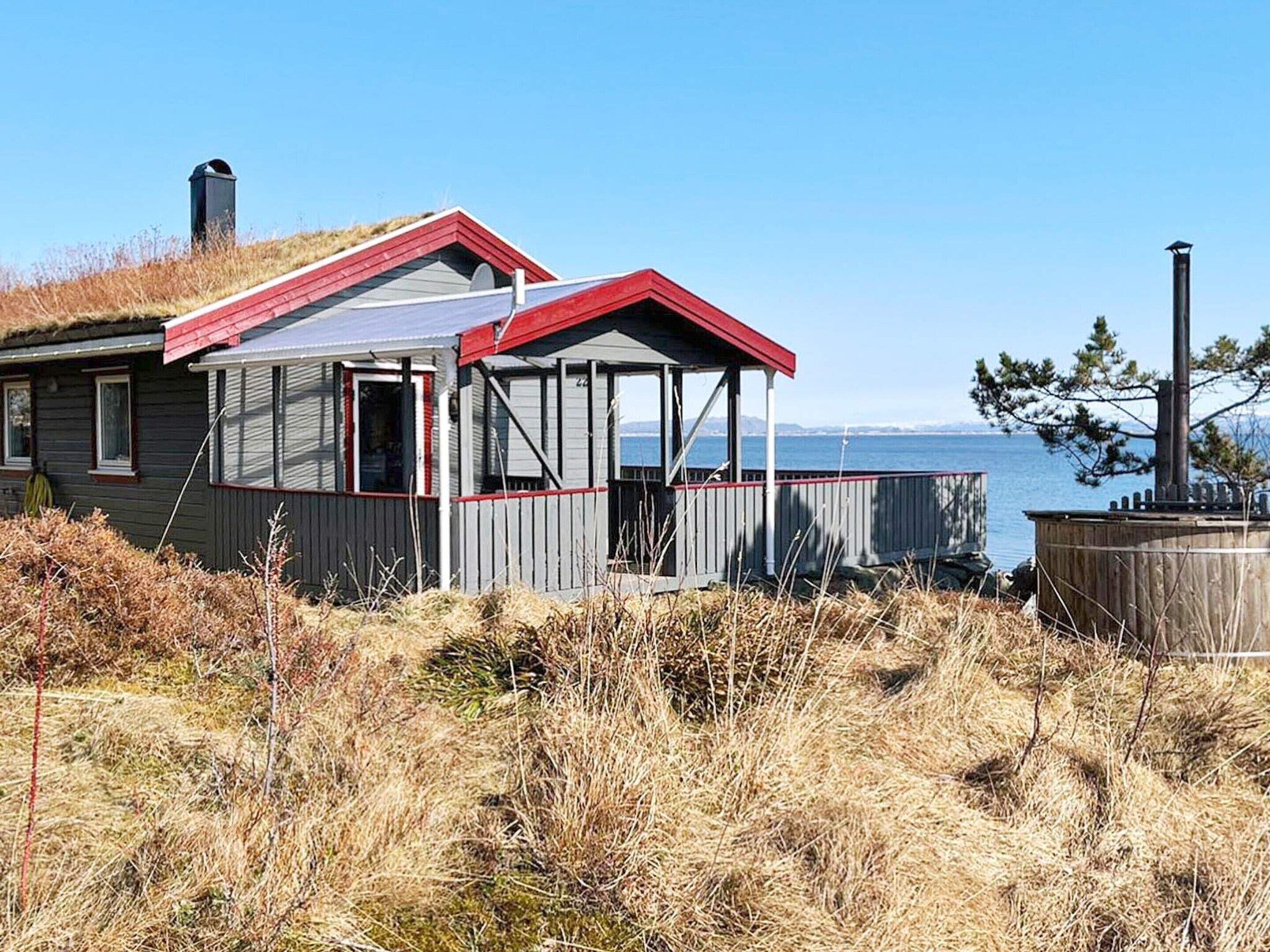 A cabin with a red roof and a covered porch, situated near a body of water.