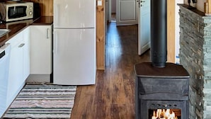 A kitchen with a wood-burning stove, white cabinets, and a microwave. - Holiday Home in Storfosna (Orland)