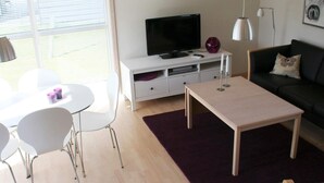 A modern living room with a TV, white furniture, a purple rug, and a black sofa. - 6 Person Holiday Home in Gudhjem-by Traum (Gudhjem)