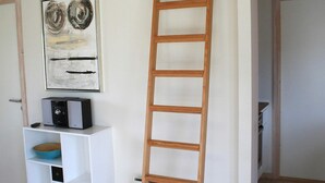 A room with a white wall, a wooden ladder, a white console table with a blue bowl, and a framed abstract painting. - 6 Person Holiday Home in Gudhjem-by Traum (Gudhjem)