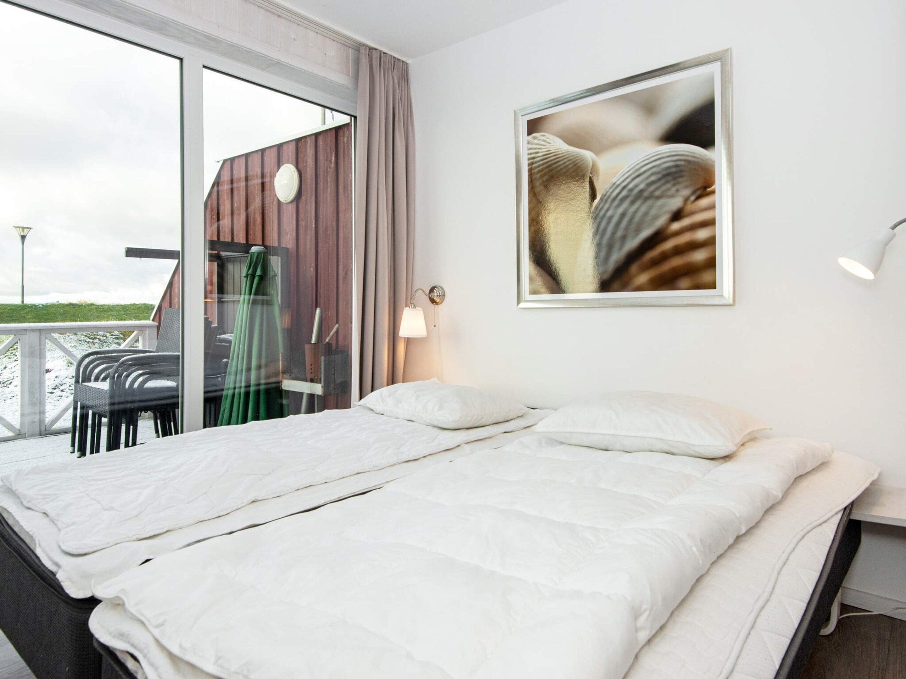 A hotel room with a large bed, a view of the outdoors, and a framed picture on the wall.