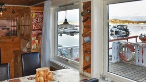 A wooden interior with a table covered in a coffee-themed tablecloth, a wooden wall with a poster, and a view of boats on water through a window. - 6 Person Holiday Home in Oksvoll (Orland)