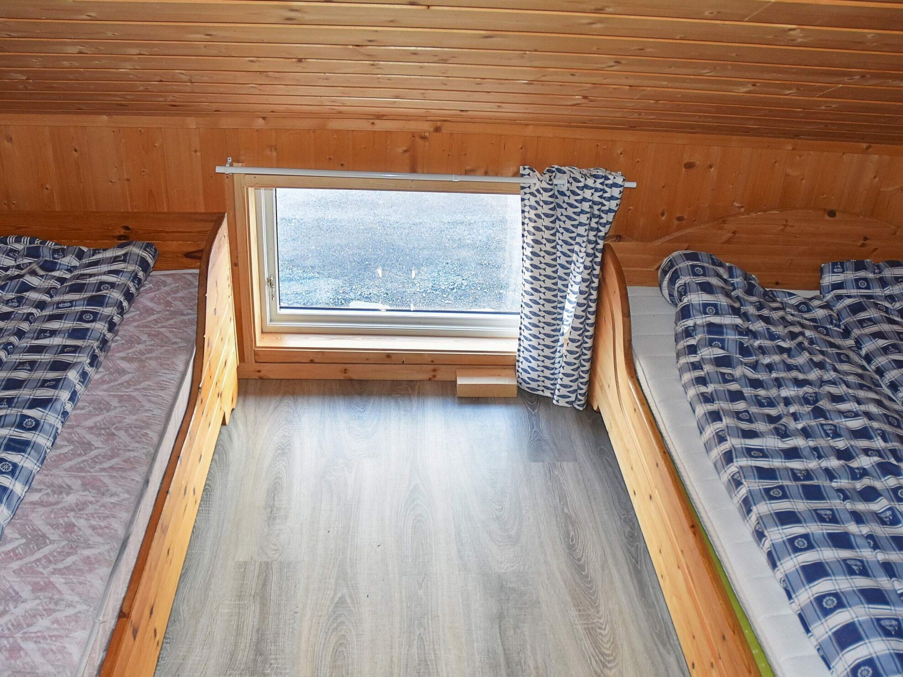 A small, wooden cabin with a single window, two beds with patterned bedding, and a wooden floor.