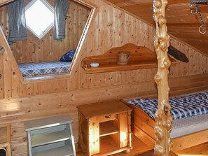 A wooden cabin with a loft bedroom, a wooden headboard, a small wooden table, and a window with curtains.