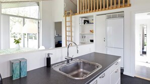 A modern kitchen with a large sink, white cabinets, and a wooden loft area. - 5 Star Holiday Home in Haderslev (Haderslev)