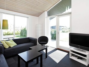 A modern living room with a sofa, a black armchair, a coffee table, a flat-screen TV, and a large window offering a view of the outdoors. - 5 Star Holiday Home in Haderslev (Haderslev)
