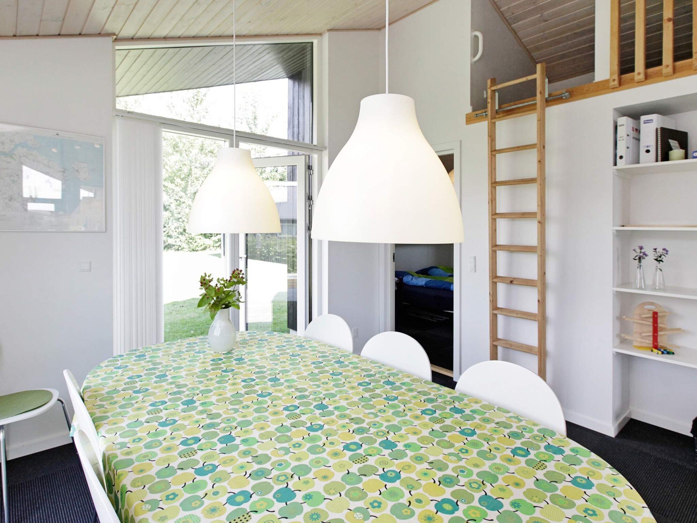 Una habitación con una mesa grande, sillas blancas, una escalera y una estantería.
