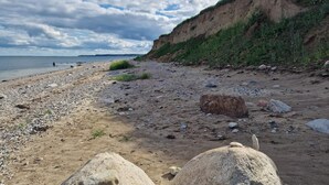 A pebbly beach with a cliff and a person in the distance. - 5 Star Holiday Home in Haderslev (Haderslev)
