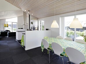 A modern kitchen with white cabinets, a dining area with a table and chairs, and a view of the outdoors through large windows. - 5 Star Holiday Home in Haderslev (Haderslev)
