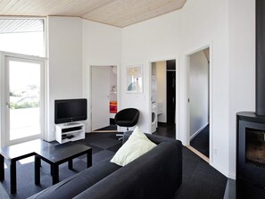A modern living room with a black sofa, a flat-screen TV on a white stand, a black coffee table, and a fireplace.
