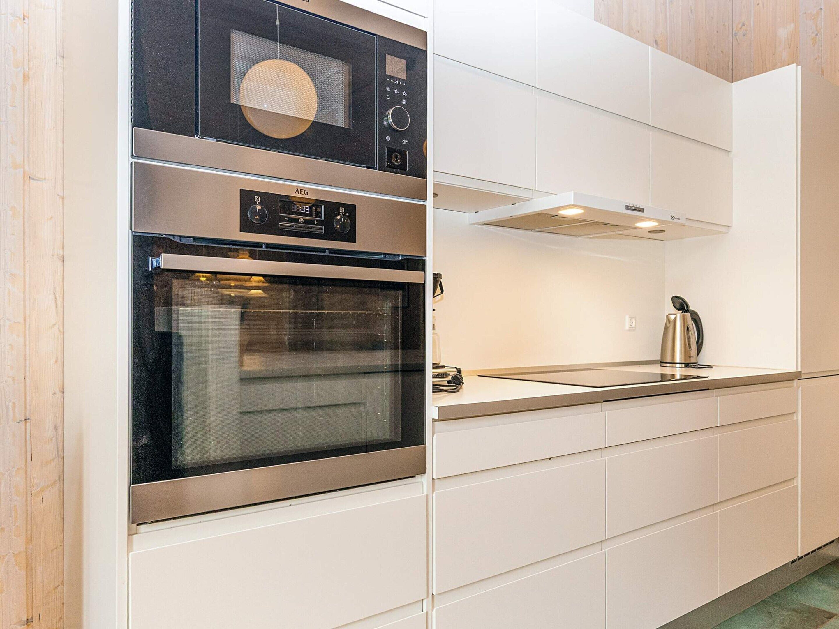 A modern kitchen with a built-in oven, a microwave, and a kettle on the countertop.