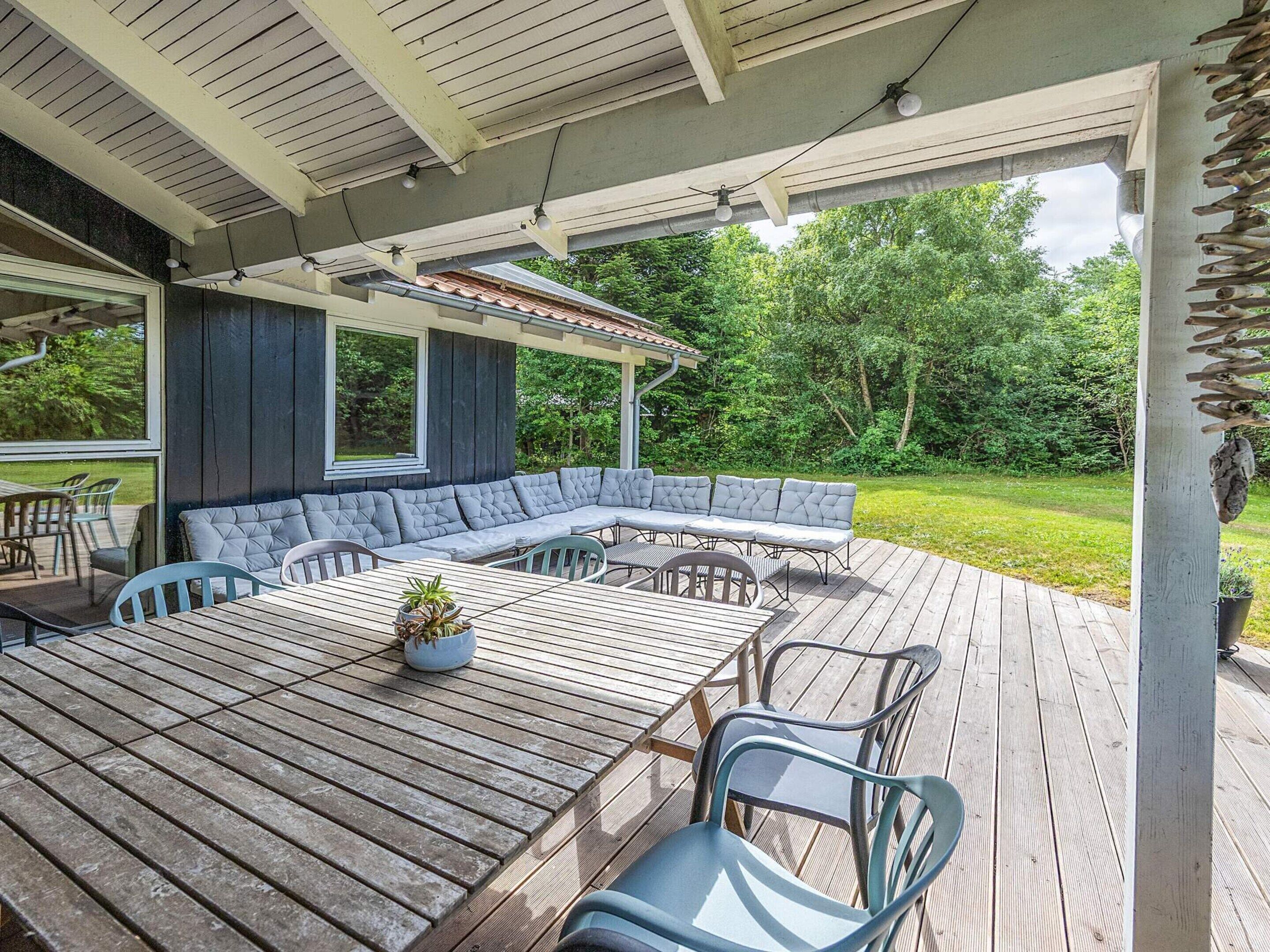 A covered outdoor dining area with a wooden deck, a large table, and a built-in bench.